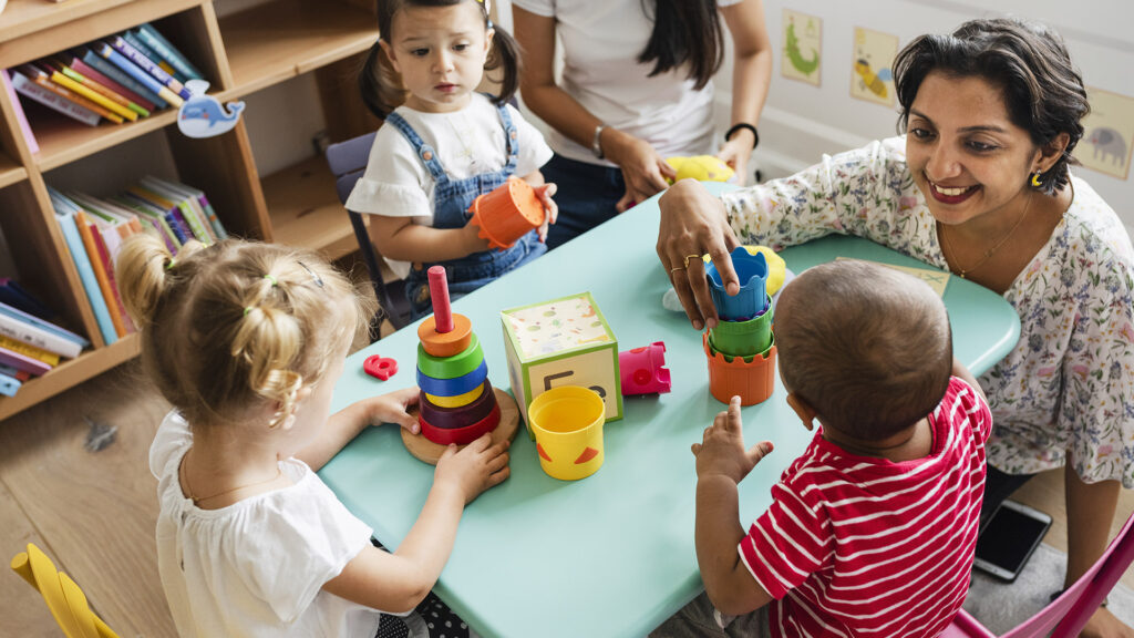 Kinder, die mit einer Betreuerin in einer Kinderkrippe spielen Krippe Und Findet